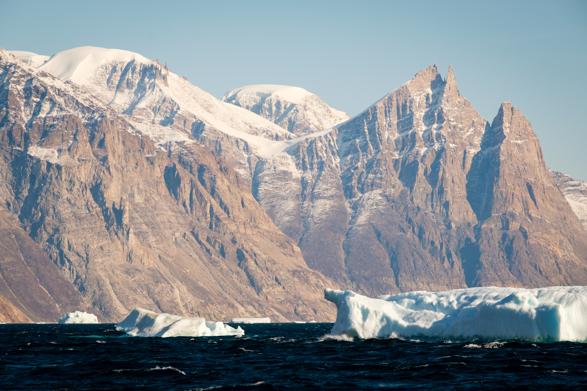 Steep mountains of Øfjord with icebergs in the front.